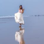 Front view of woman wearing the off-white Madhubala hand-painted portrait dress with reflection on wet beach sand.