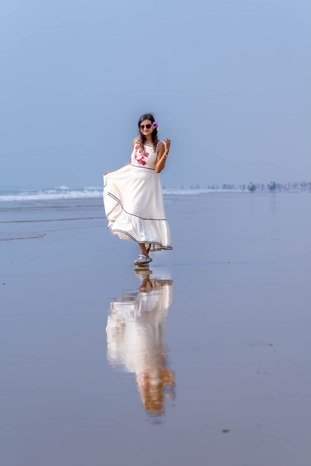 Front view of woman wearing the off-white Madhubala hand-painted portrait dress with reflection on wet beach sand.