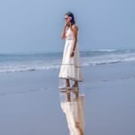 Side profile of woman wearing the sleeveless white Madhubala handpainted dress with ocean background.