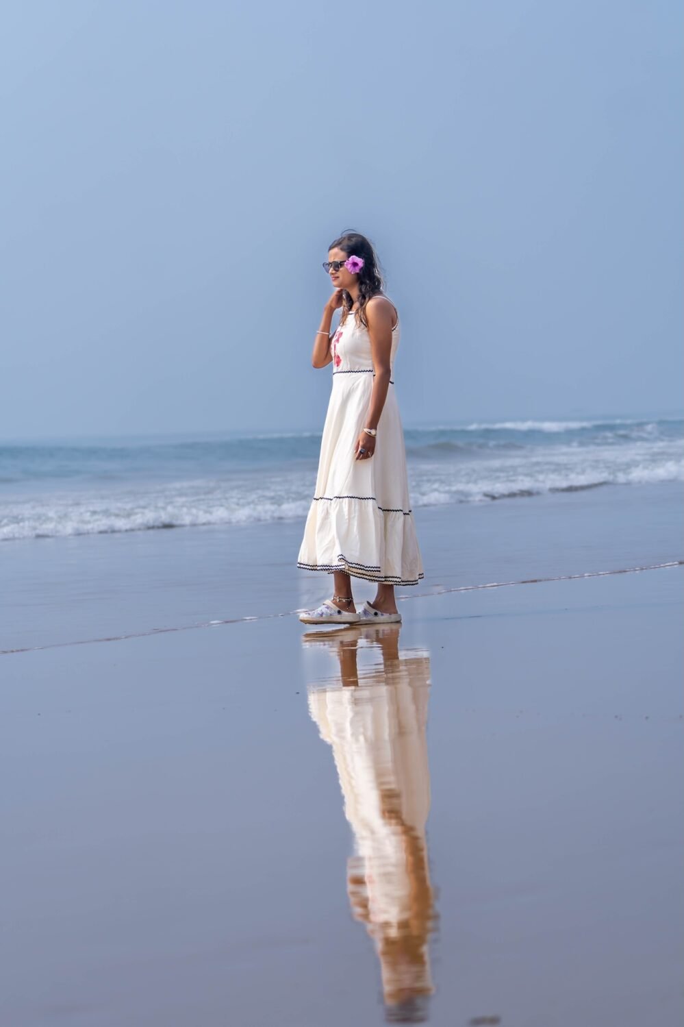 Side profile of woman wearing the sleeveless white Madhubala handpainted dress with ocean background.