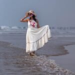 Woman wading through sea waves wearing the flared Madhubala hand-painted dress and sun hat.
