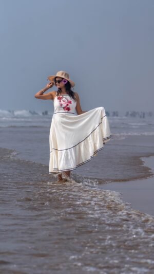 Woman wading through sea waves wearing the flared Madhubala hand-painted dress and sun hat.