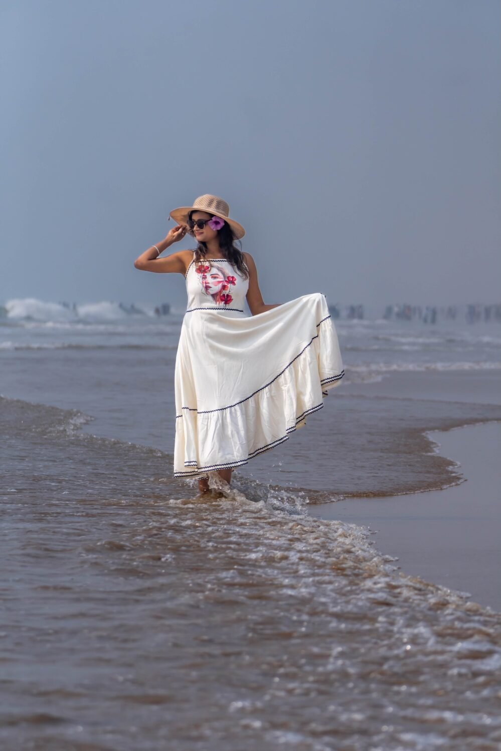 Woman wading through sea waves wearing the flared Madhubala hand-painted dress and sun hat.