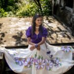Model sitting outdoors with the Nilaambari off-white lehenga skirt fully spread out to reveal the complete handpainted floral design.