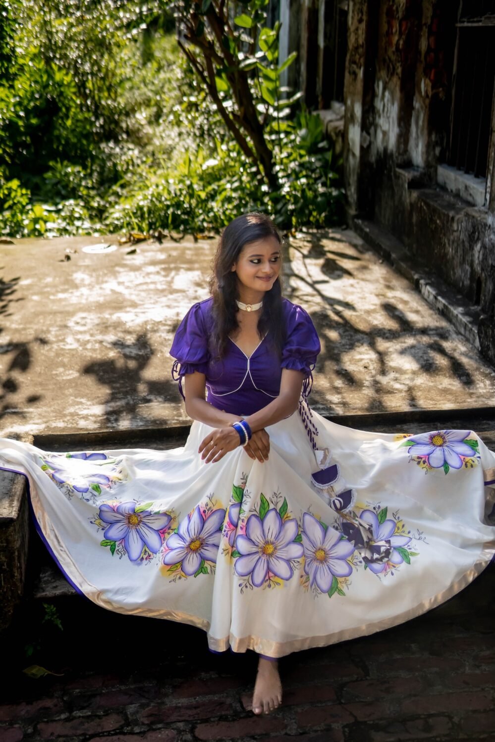 Model sitting outdoors with the Nilaambari off-white lehenga skirt fully spread out to reveal the complete handpainted floral design.