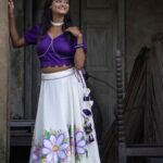 Model standing at an architectural doorway wearing the Nilaambari off-white handpainted lehenga and violet scalloped blouse set by Aankibukis Couture.