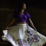 Model twirling in the Nilaambari off-white flared lehenga skirt showcasing the circular handpainted floral pattern and gold border.