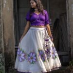 Front view of the Nilaambari cotton lehenga set showing the wide flared off-white skirt with handpainted purple floral motifs and dark violet top.