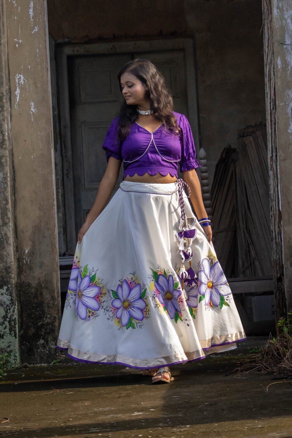 Front view of the Nilaambari cotton lehenga set showing the wide flared off-white skirt with handpainted purple floral motifs and dark violet top.