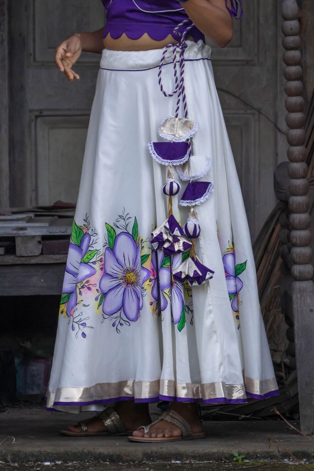 Close-up detail of the handcrafted purple and white waist tassels and handpainted floral hemline on the Nilaambari lehenga skirt.