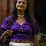 Close-up shot of the Nilaambari deep violet blouse featuring a scalloped hemline, deep V-neckline, white piping, and tie-up puff sleeves.