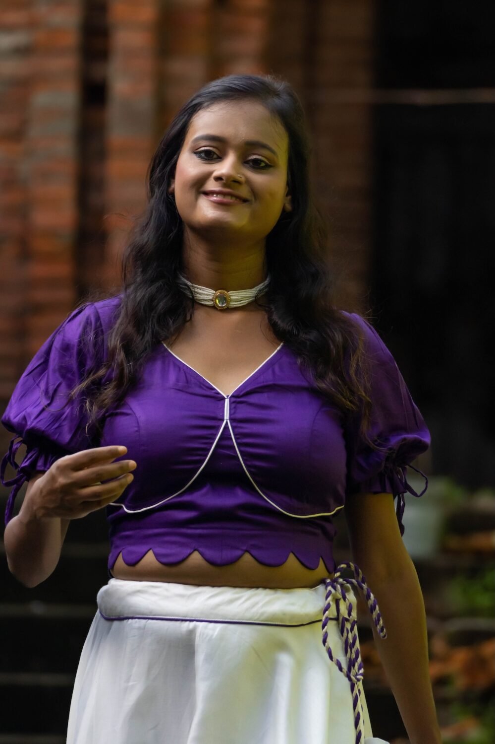 Close-up shot of the Nilaambari deep violet blouse featuring a scalloped hemline, deep V-neckline, white piping, and tie-up puff sleeves.