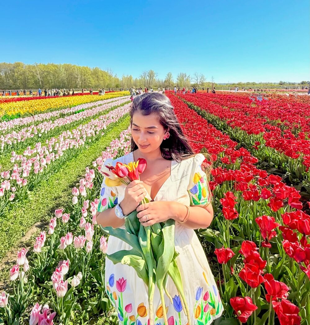 Woman smiling softly while holding a tulip bouquet in a field of red and pink flowers wearing a handpainted off-white dress