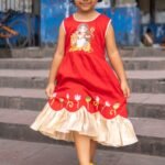 Little girl holding out the flared skirt of the red handpainted Durga Rani kids ethnic dress.