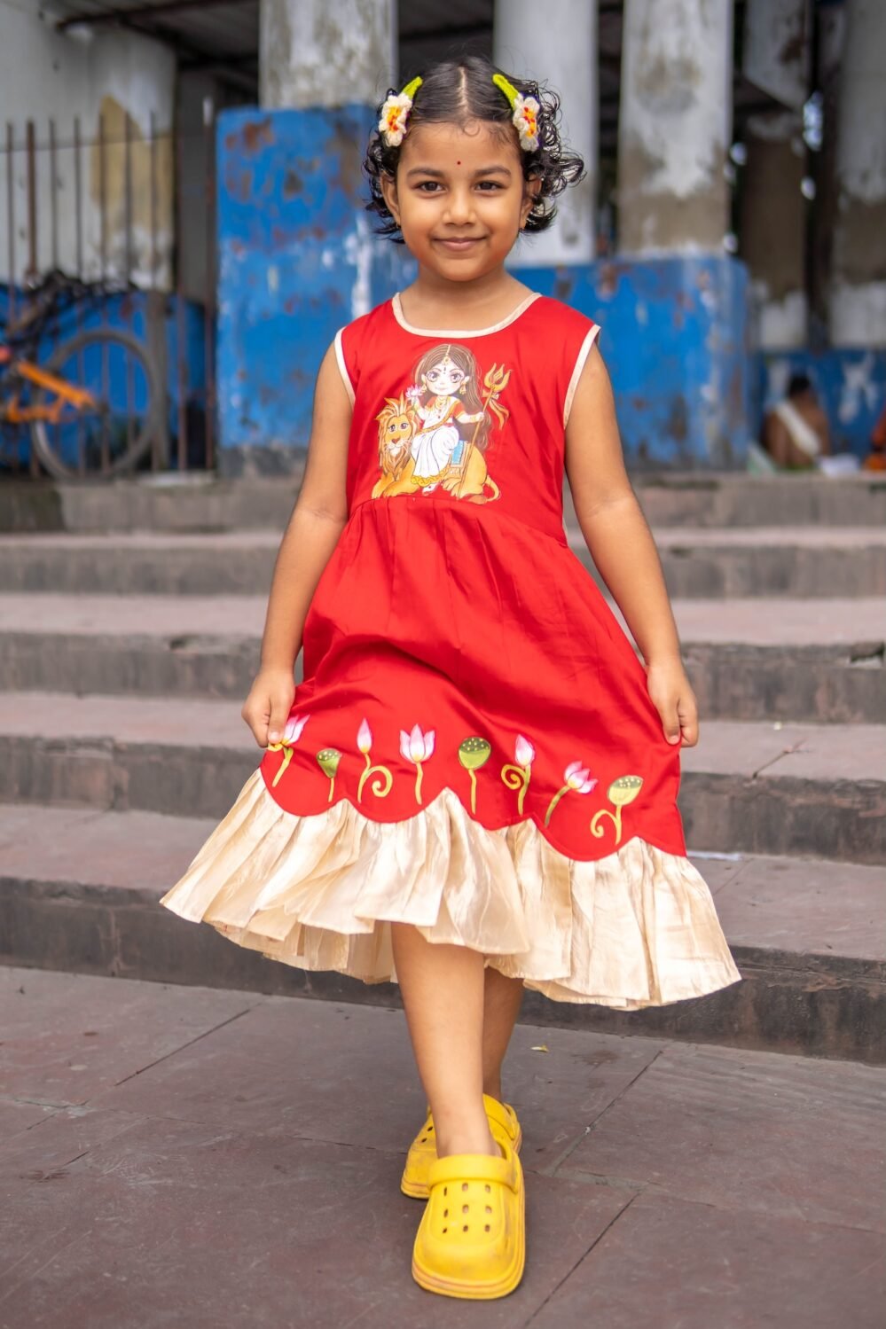 Little girl holding out the flared skirt of the red handpainted Durga Rani kids ethnic dress.
