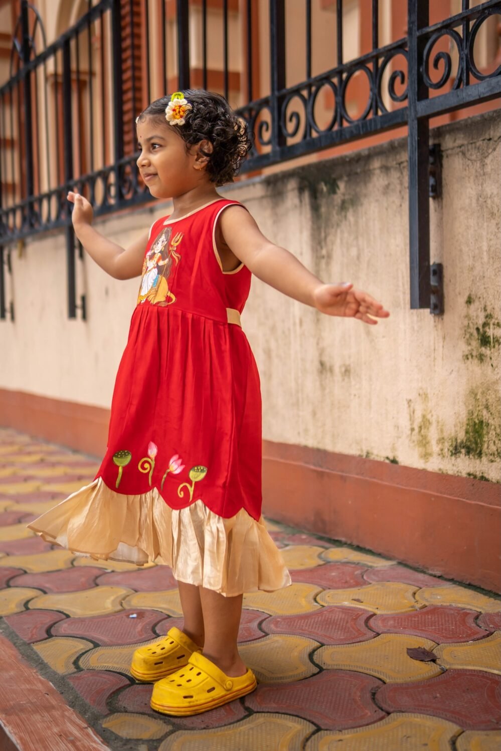 Side view of little girl dancing outdoors wearing sleeveless handpainted Durga Rani ethnic frock.
