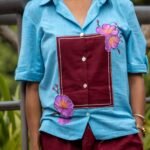 Close-up detail of the handpainted 3D purple orchids and maroon kantha stitch patch on the sky blue cotton shirt.
