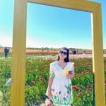 Woman wearing the handpainted tulip short dress by Aankibukis Couture posing inside a large yellow decorative frame in a garden