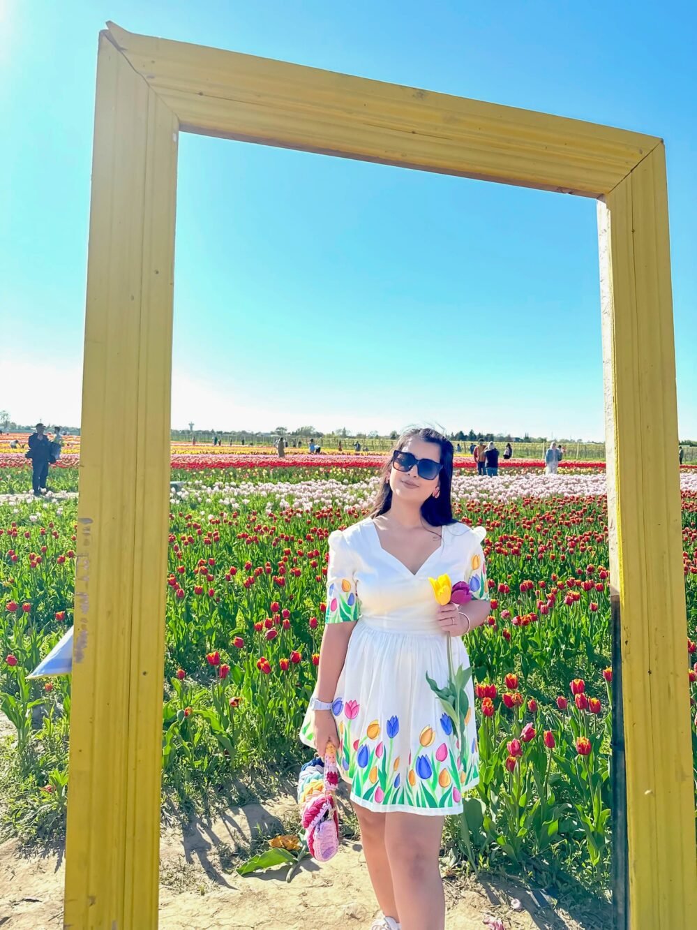 Woman wearing the handpainted tulip short dress by Aankibukis Couture posing inside a large yellow decorative frame in a garden