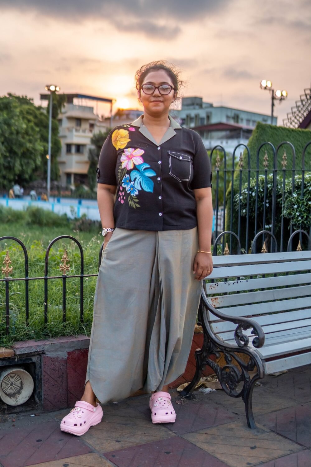 Full-length shot of a woman walking outdoors in a black hand-painted handloom cotton top and relaxed sage green urban dhoti trousers