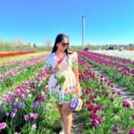 Full-length view of a woman walking through purple and white tulip rows in an off-white handpainted cotton dress