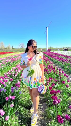 Full-length view of a woman walking through purple and white tulip rows in an off-white handpainted cotton dress