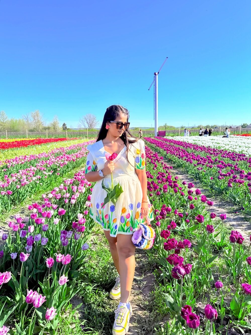 Full-length view of a woman walking through purple and white tulip rows in an off-white handpainted cotton dress