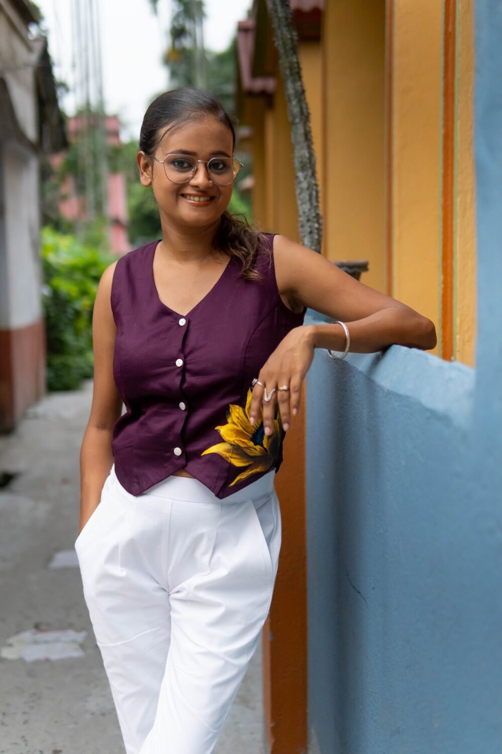 Full styling shot of a woman wearing a purple handpainted waist coat styled as a top with white trousers.