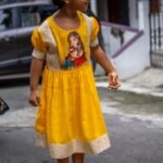 Side view of a girl posing in the yellow handpainted Durga Dulali frock showing puff sleeves and brocade highlights.