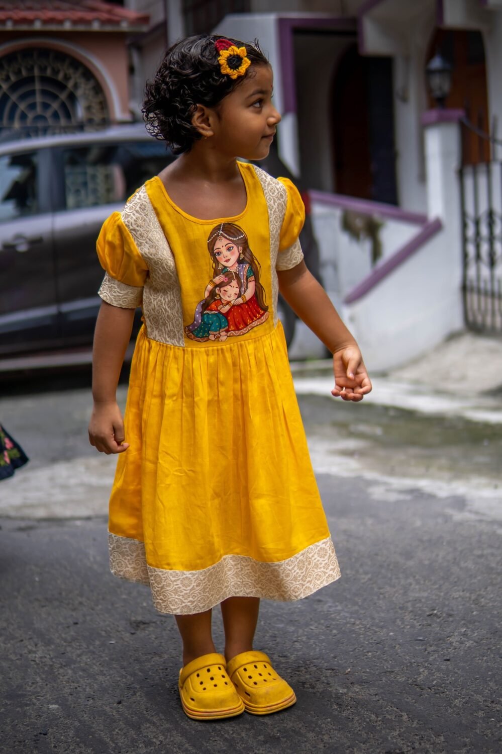 Side view of a girl posing in the yellow handpainted Durga Dulali frock showing puff sleeves and brocade highlights.