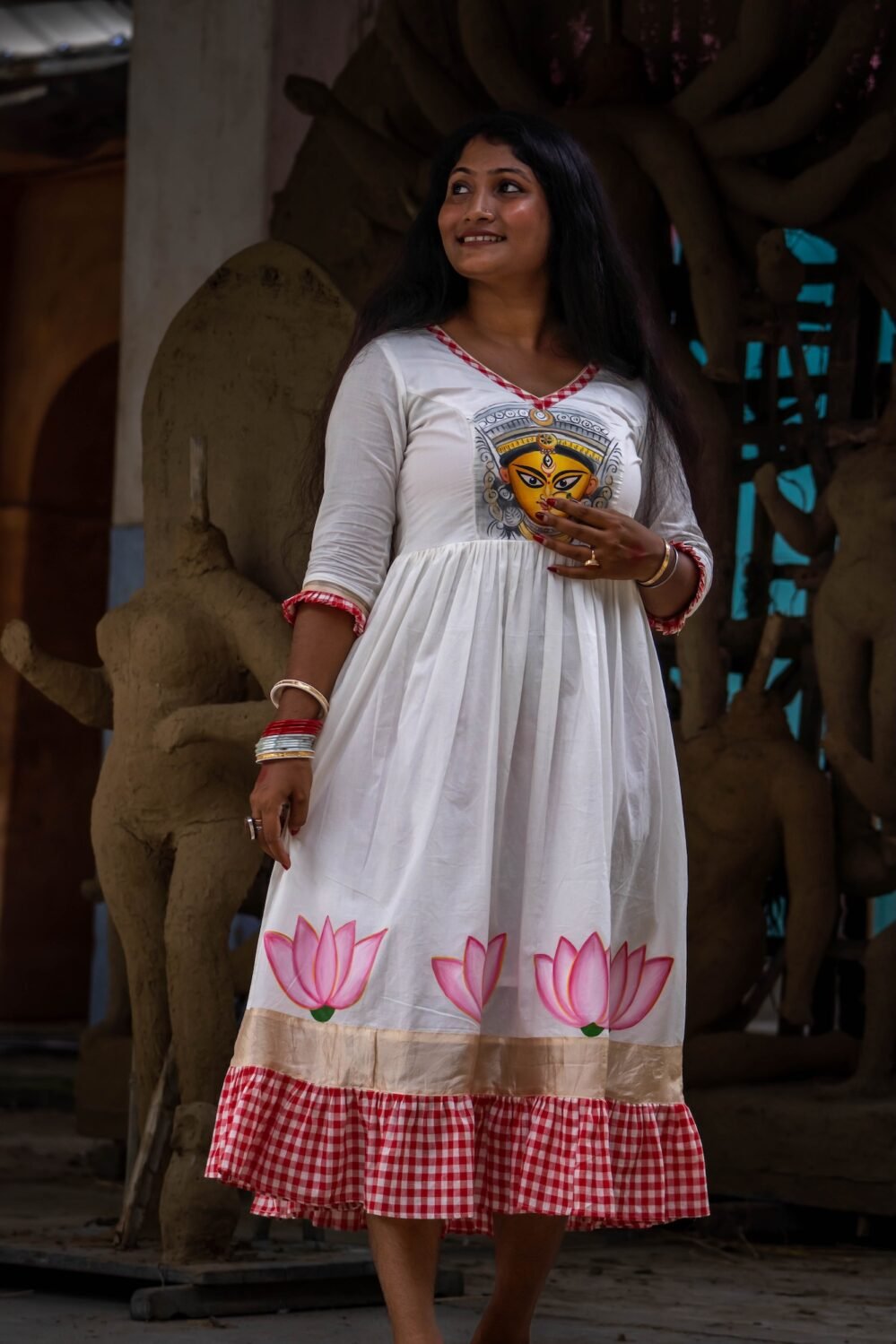Full shot of a woman in the Annapurna hand-painted dress standing against clay Durga sculptures.