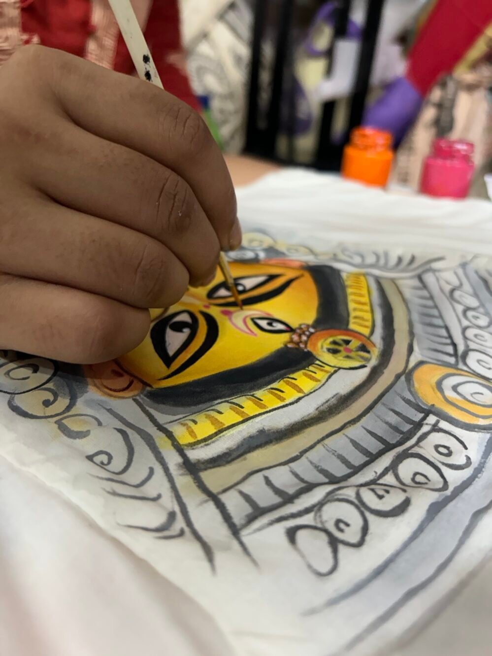 Artist hand-painting the fine eye details of the Maa Durga motif on white fabric with a thin paintbrush.