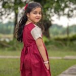 Back view of a little girl wearing the maroon Chhoto Uma cotton frock showing the tied back sash and short cream sleeves.