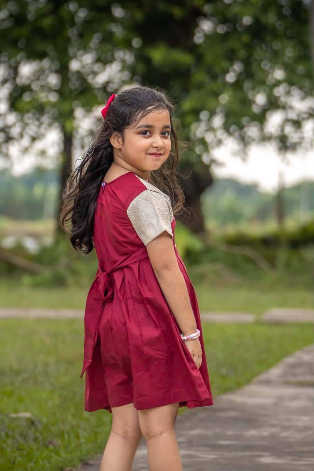 Back view of a little girl wearing the maroon Chhoto Uma cotton frock showing the tied back sash and short cream sleeves.