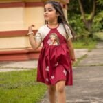 Little girl walking outdoors while wearing the maroon Chhoto Uma handpainted pure cotton frock for Durga Puj