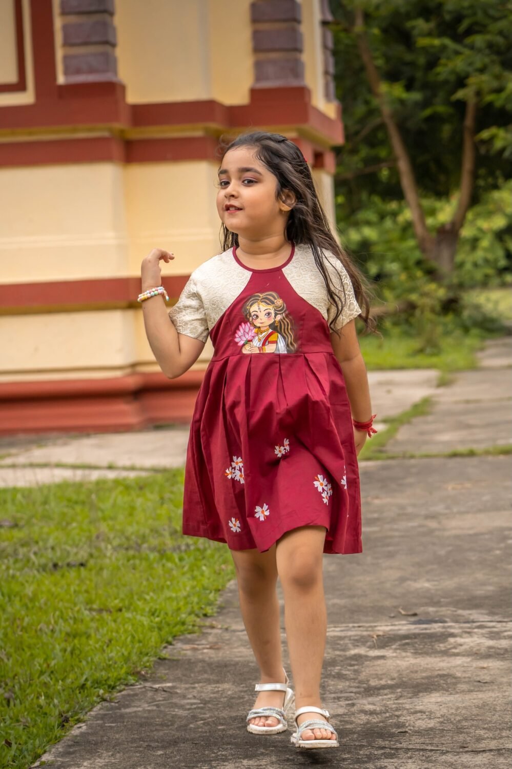 Little girl walking outdoors while wearing the maroon Chhoto Uma handpainted pure cotton frock for Durga Puj