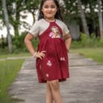 Full view of a young girl standing in the maroon handpainted Chhoto Uma cotton frock by Aankibukis Couture.