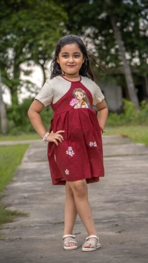 Full view of a young girl standing in the maroon handpainted Chhoto Uma cotton frock by Aankibukis Couture.