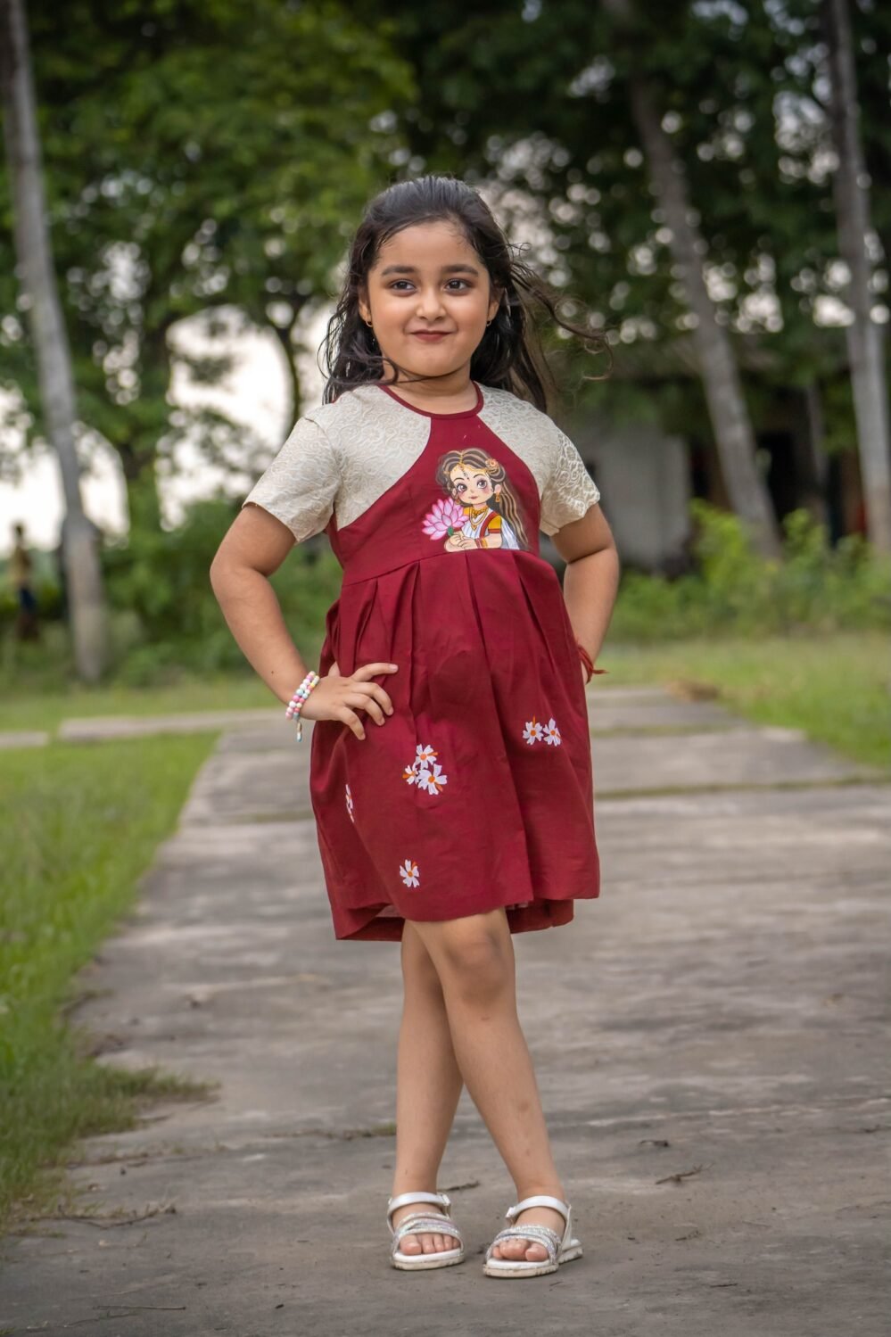 Full view of a young girl standing in the maroon handpainted Chhoto Uma cotton frock by Aankibukis Couture.