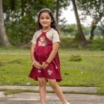 Full-length outdoor image of a little girl posing in the maroon Chhoto Uma pure cotton handpainted festive frock.