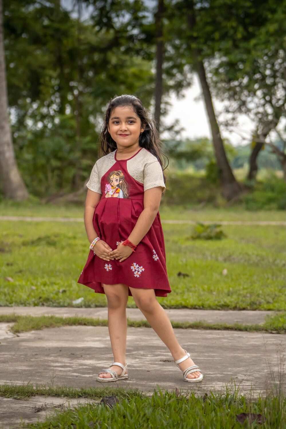 Full-length outdoor image of a little girl posing in the maroon Chhoto Uma pure cotton handpainted festive frock.