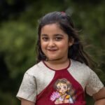 Portrait shot of a smiling girl in the handpainted Chhoto Uma maroon pure cotton frock by Aankibukis Couture.