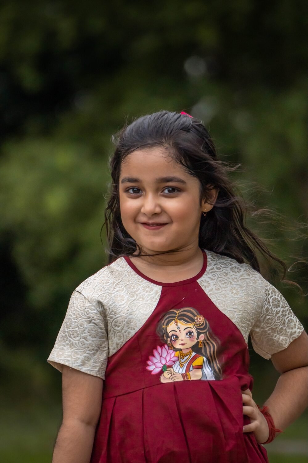 Portrait shot of a smiling girl in the handpainted Chhoto Uma maroon pure cotton frock by Aankibukis Couture.