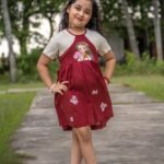 Full-length shot of a girl wearing the maroon handpainted Chhoto Uma pure cotton frock with white floral detailing on the skirt.