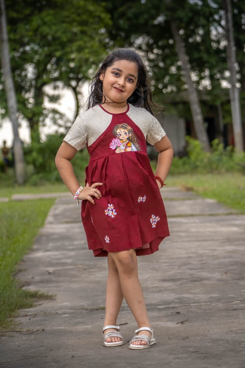 Full-length shot of a girl wearing the maroon handpainted Chhoto Uma pure cotton frock with white floral detailing on the skirt.