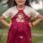 Front pose of a girl wearing the handpainted Chhoto Uma maroon frock showcasing the Maa Durga motif and pleated skirt design.
