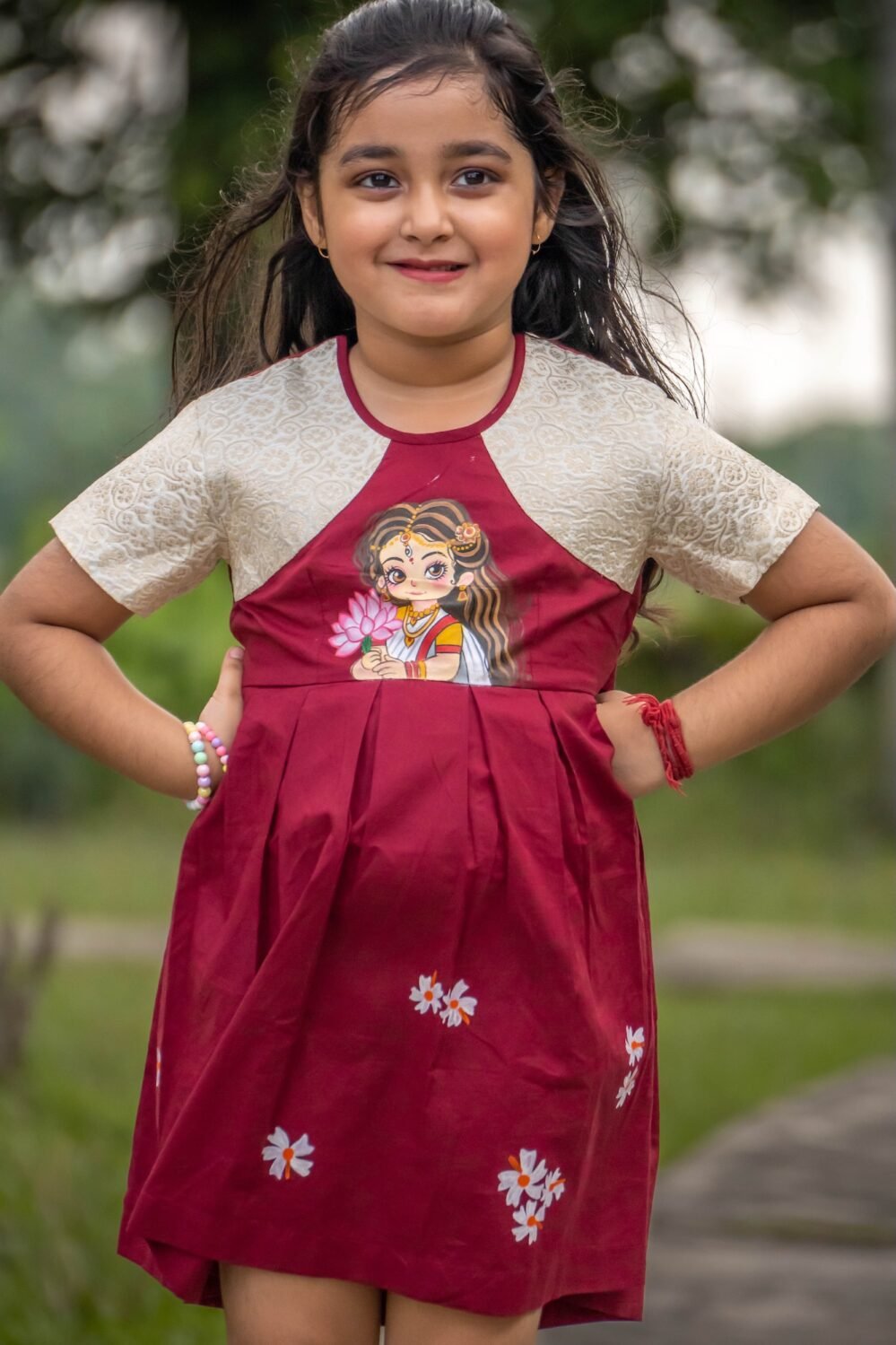 Front pose of a girl wearing the handpainted Chhoto Uma maroon frock showcasing the Maa Durga motif and pleated skirt design.