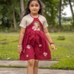 Front full shot of a girl modeling the maroon and cream Chhoto Uma handpainted frock with small white flower details.