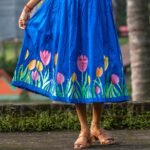 Close-up detail of hand-painted pink, orange, and yellow tulips on the hem of a royal blue dress.