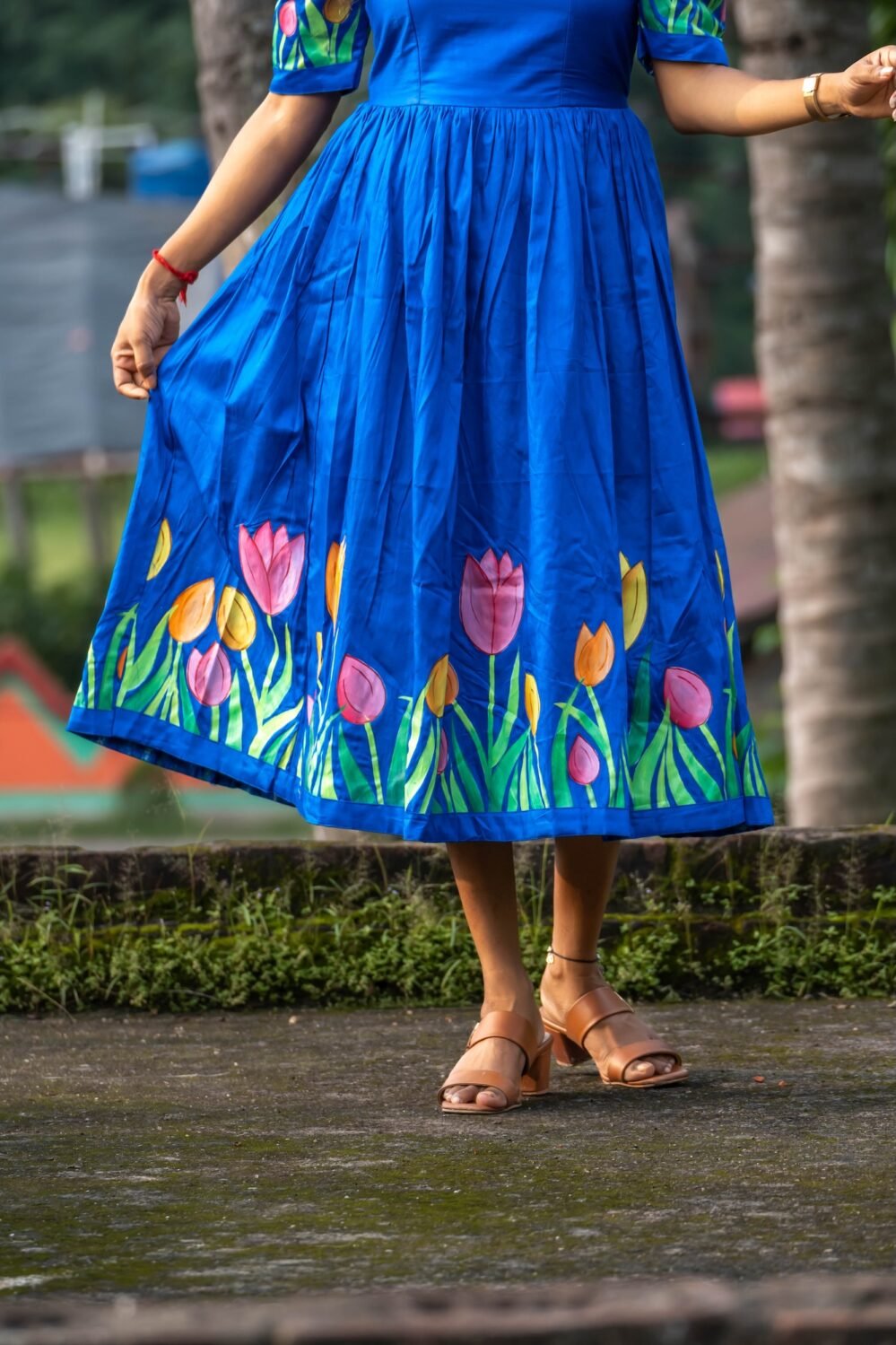 Close-up detail of hand-painted pink, orange, and yellow tulips on the hem of a royal blue dress.